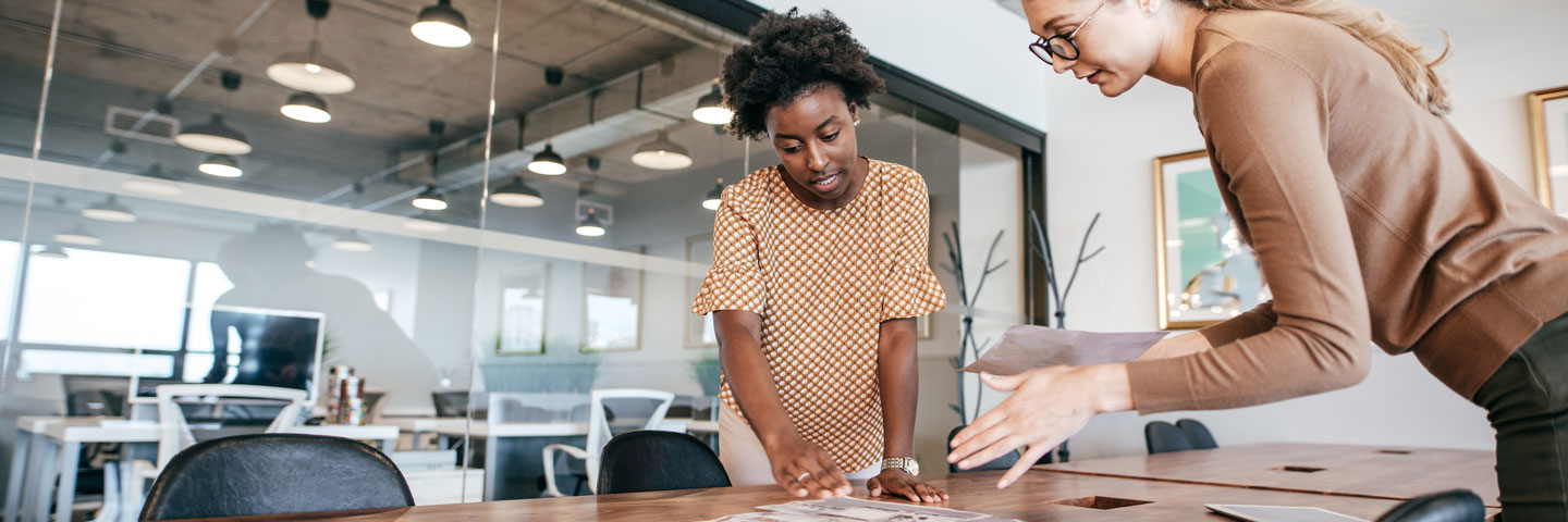 Two people studying documents spread across a conference table 