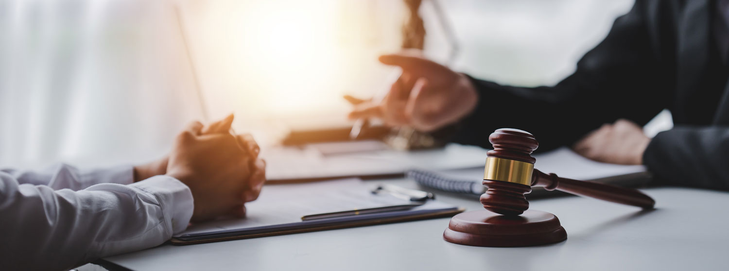 A gavel on a desk with a persons arm and hand showing in the background pointing toward another person