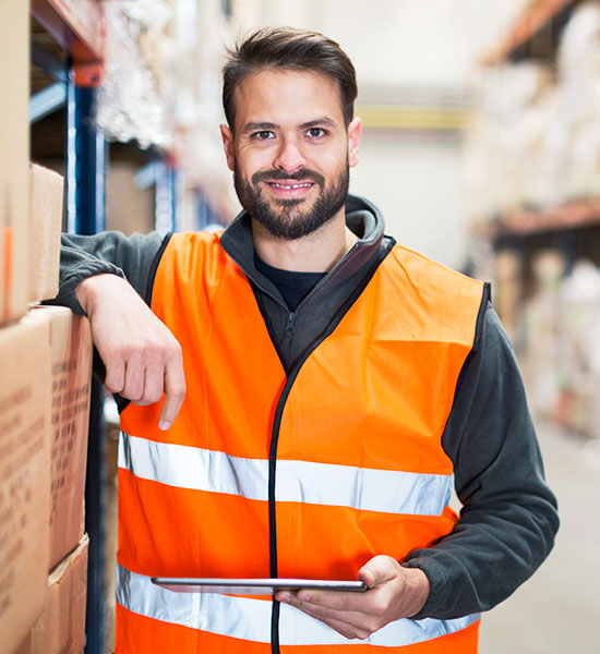 Guy wearing a safety vest holding a clip board standing in a warehouse